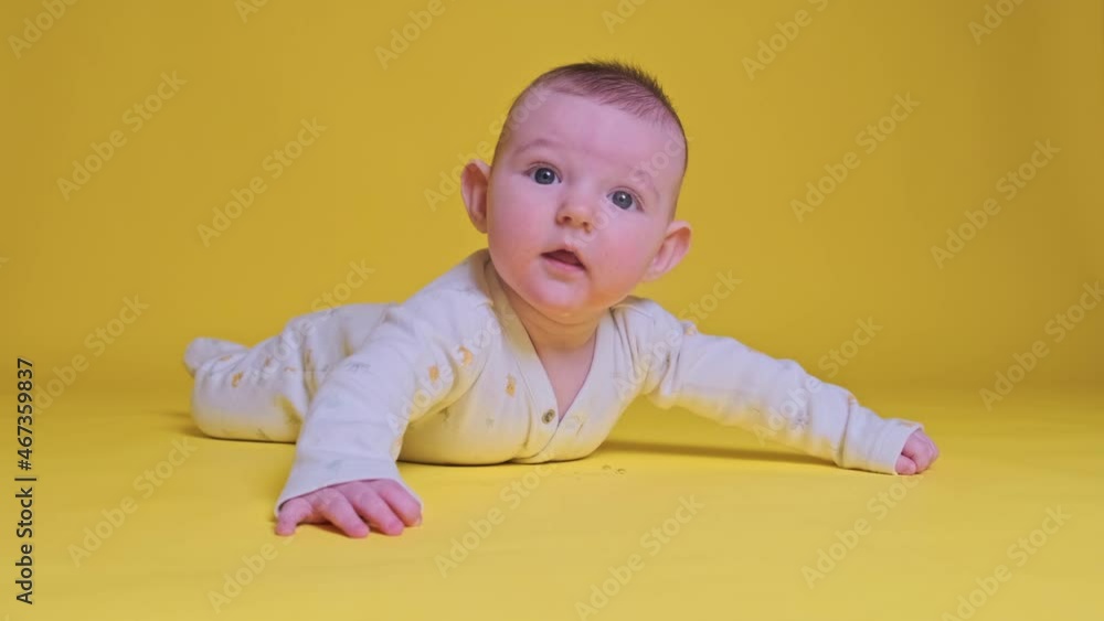 Happy infant baby boy looks in surprise and laughing lying on his tummy, yellow studio background. Four month old child close up Happy infant baby boy looks in surprise and laughing lying on his tummy, yellow studio background. Four month old child close up