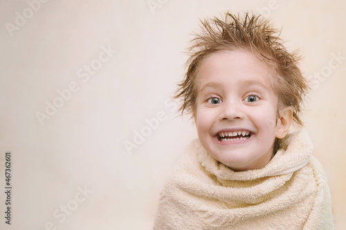 Close-up portrait of joyful cute caucasian little boy looking at camera, toothy smiling, wrapped in orange towel with wet hair. Horizontal shot with copy space. Children hygien concept