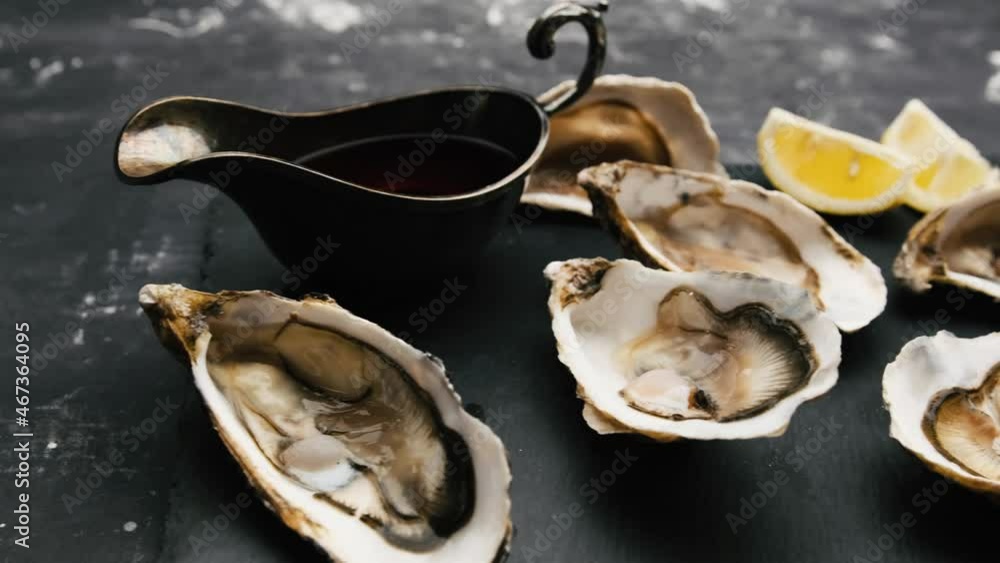Raw oysters with lemon and bowl of sauce on black plate. Luxury seafood Raw oysters with lemon and bowl of sauce on black plate. Luxury seafood