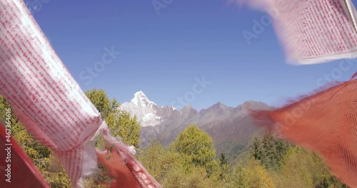 Close up of colourful Tibetan praying flags swaying in the wind with snow mountain peak in th background at four girls mountain park of Sichuan China photo