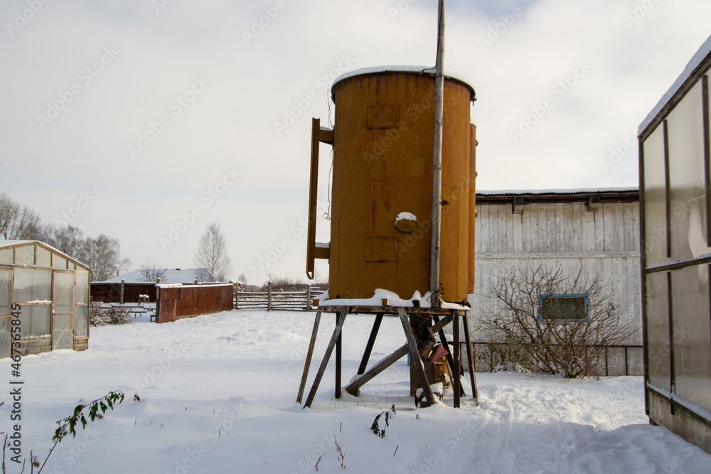 Large old rusty watering barrel on high supports in the courtyard of a country house on a farm Large old rusty watering barrel on high supports in the courtyard of a country house on a farm