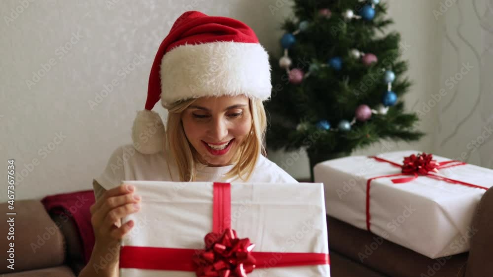 Close-up shot of Happy adorable woman in Santa Claus hat opening her Christmas present. Cozy Christmas interior. Winter holidays	