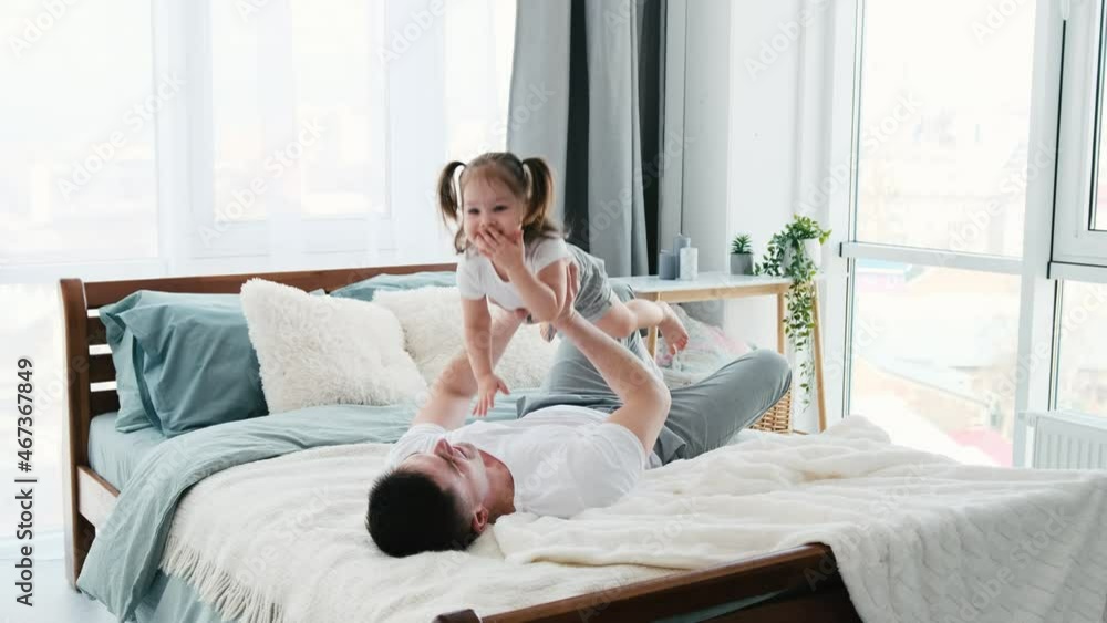 Beautiful family morning together in the bed in sunny apartment. Father playing with little daughter in the bedroom throwing her up. Dad with kid and dog in the room with daylight. Beautiful family morning together in the bed in sunny apartment. Father playing with little daughter in the bedroom throwing her up. Dad with kid and dog in the room with daylight.