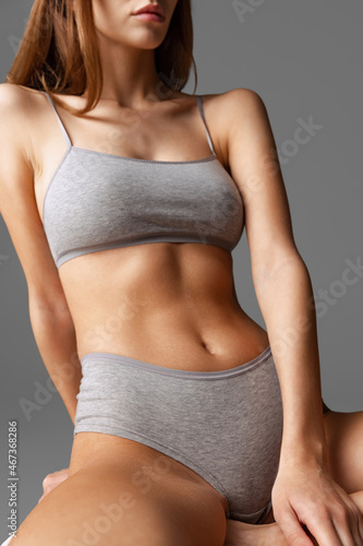 Beautiful body of young slim woman in grey underwear isolated on gray studio background. Natural beauty concept. Bottom view