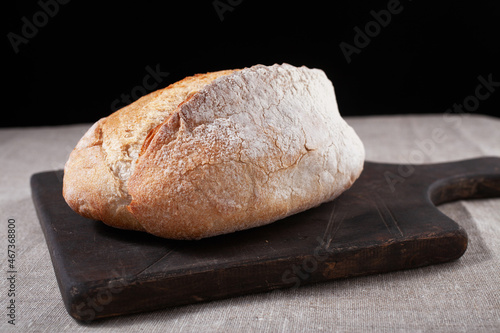ciabatta of wheat flour on a tree stand close-up on a black background. Baking, flour, bread