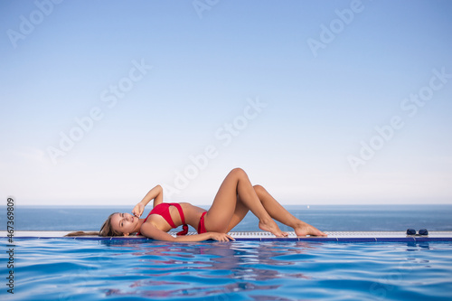 Photos Young woman relaxing in infinity swimming pool looking at view