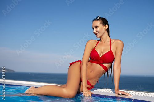 Картината върху платно Young woman relaxing in infinity swimming pool looking at view