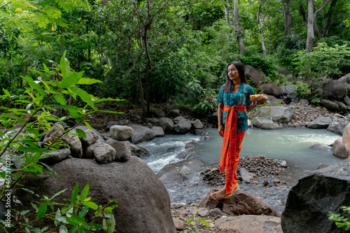 Portrait of a beautiful asian girl by the river in a brightly colored suit and offerings in hand. 