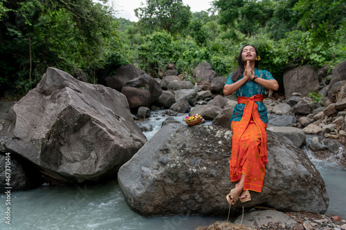 Praying girl by the river in a traditional brightly colored suit and offerings in hand. 