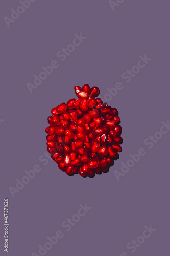 Ripe red pomegranate seeds stacked in the shape of a pomegranate, on a purple background, isolited, Whole fruit shaped pomegranate seeds. photo