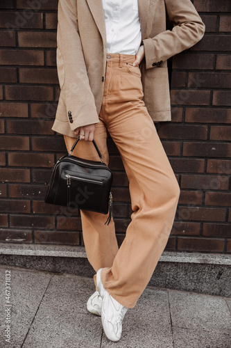 Tall stylish girl with a bag in a beige oversized jacket and orange pants on brick wall background