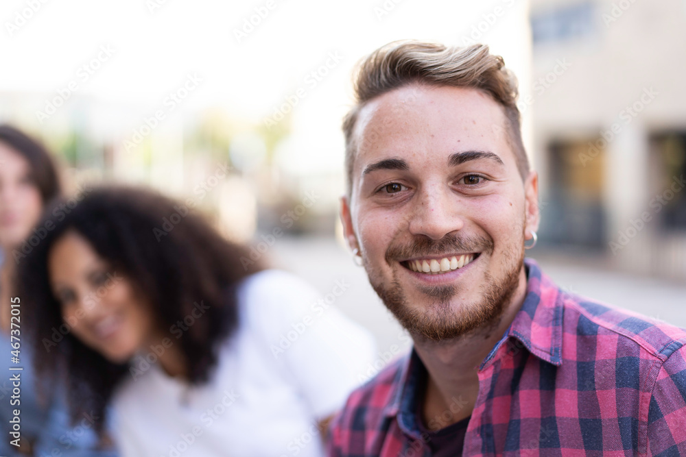 Young man smiling on camera having fun outdoor with multiracial friends in the city - Focus on face Young man smiling on camera having fun outdoor with multiracial friends in the city - Focus on face