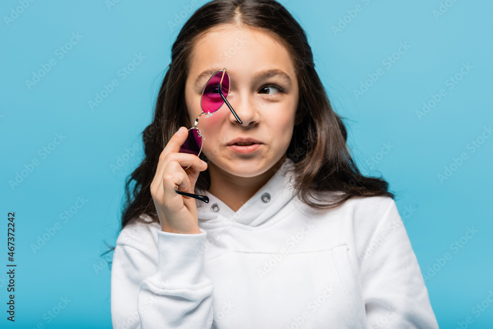 preteen girl holding pink sunglasses isolated on blue. preteen girl holding pink sunglasses isolated on blue.