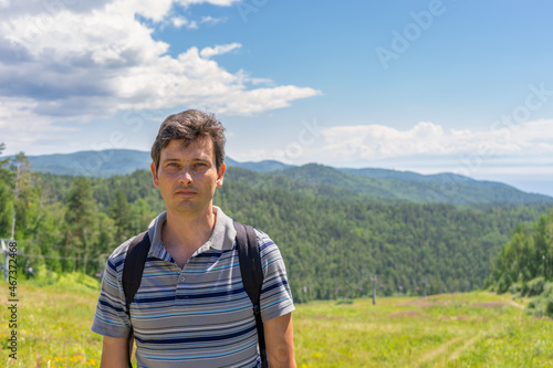Portrait of handsome middle aged tourist man against beautiful mountain landscape in summer sunny day. View from hill to cable way between Listvyanka and Chersky stone. Lake Baikal, Siberia, Russia