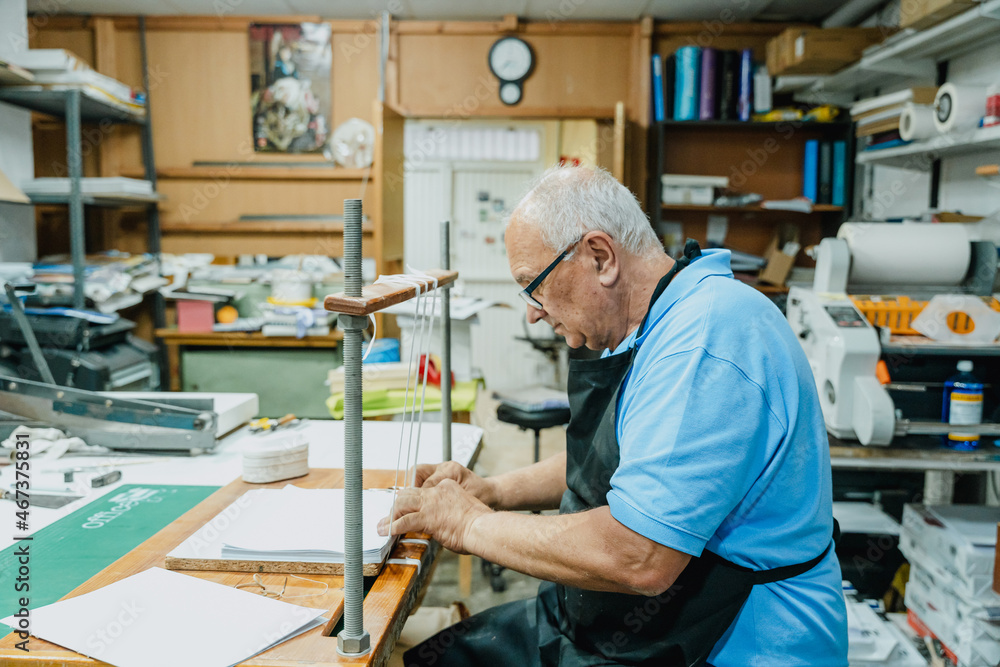 Focused aged male artisan tying tapes on wooden board in printing studio Focused aged male artisan tying tapes on wooden board in printing studio