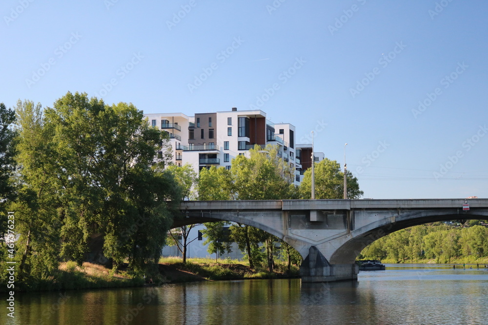 Elegant bridge over the Vltava River surrounded by green trees against a blue sky on a clear day