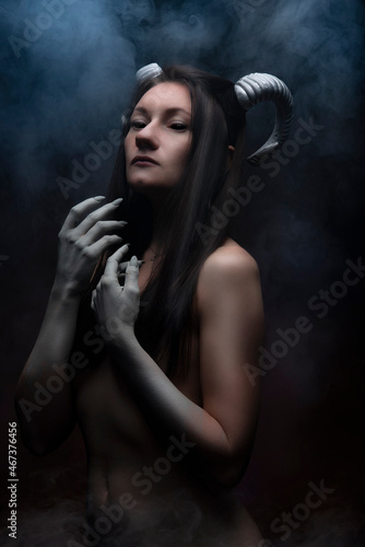 Halloween holiday. A girl with horns and black eyes in the smoke. Demon, smoke, fear, fantasy