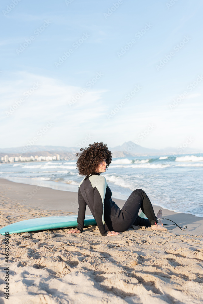 Woman in wetsuit with surfboard lying on sandy beach Woman in wetsuit with surfboard lying on sandy beach