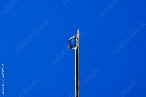 a drop of solution at the end of a medical syringe on a blue background macro. Medicine injection medicine health