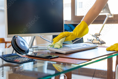 Unrecognizable woman in gloves cleaning working desk with modern computer photo