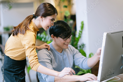 Candid of young Asian businesswoman looking at computer monitor discussing marketing online results with young creative Asian worker on project. Coworkers discuss online project teamwork in office © edward_indy