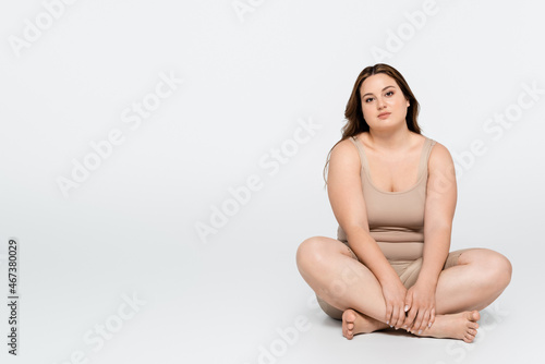 Brunette woman with overweight sitting with crossed legs on grey background.
