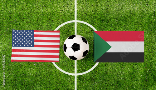 Top view soccer ball with USA vs. Sudan flags match on green football field.
