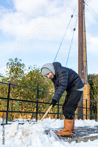 A young man clearing the footpath of snow and ice to make it safe to walk on during a heavy snowfall. Winter safety, clearing snow and ice concept