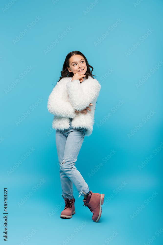 full length of cheerful preteen girl in faux fur jacket posing on blue ...