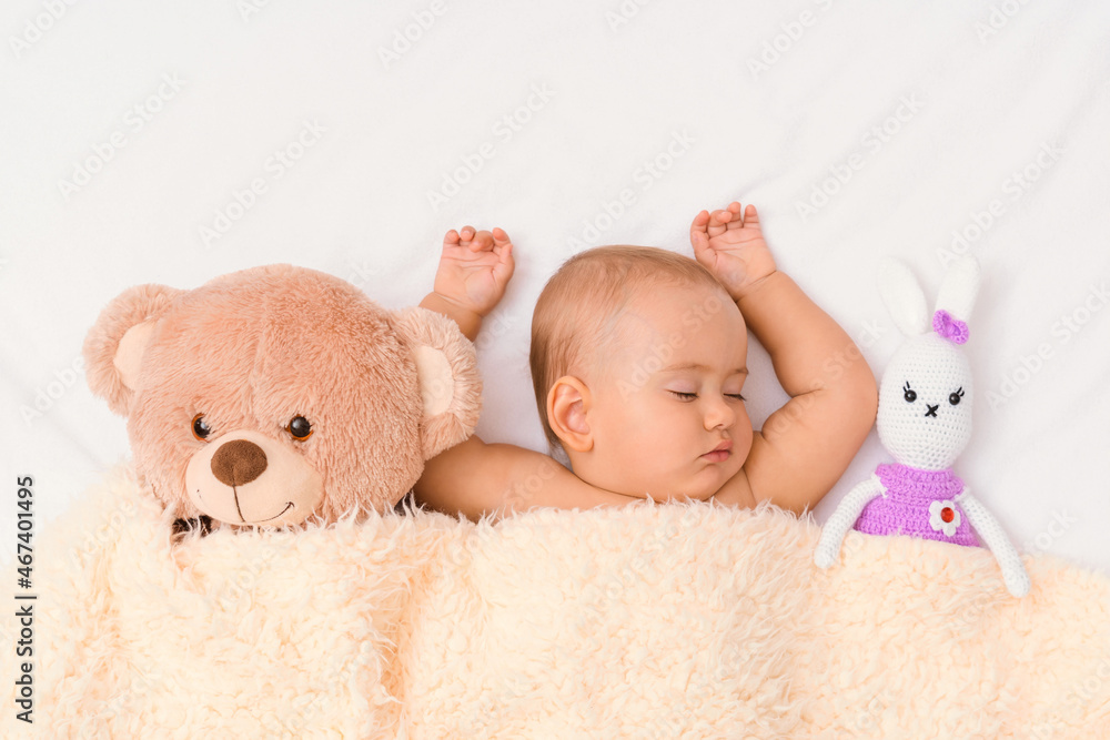 The baby sleeps with his favorite toys, a teddy bear and a knitted hare. Newborn sleeping under a blanket, top view The baby sleeps with his favorite toys, a teddy bear and a knitted hare. Newborn sleeping under a blanket, top view