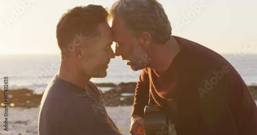Happy caucasian gay male couple sitting on car playing guitar and kissing at the beach