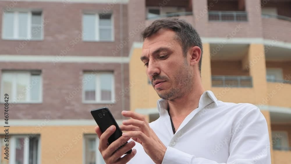 Close-up of a businessman working intently in a smartphone. Young man in the city center against the background of high-rise buildings. The concept of business and professional activities. 4K UHD. Close-up of a businessman working intently in a smartphone. Young man in the city center against the background of high-rise buildings. The concept of business and professional activities. 4K UHD.