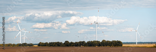 Rotating wind generators in the field against the cloudy sky on sunny summer day. Panoramic view.