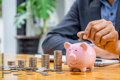 A businessman puts a coin in a piggy bank . A man saves money for household expenses. utility bills Monthly Family Budget Calculation Investment or personal savings strategy.