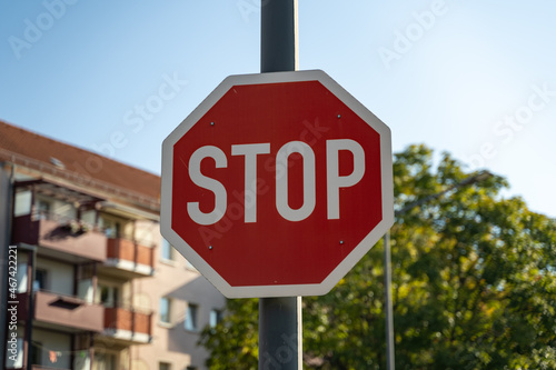 A stop sign in front of a tree and a residential building on a sunny day. Traffic symbols in a German city to make car drivers cautious and careful to prevent accidents.