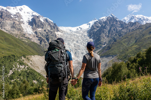 A couple enjoying the panoramic view on the snow-capped peaks of Tetnuldi, Gistola, Lakutsia and the Adishi Glacier in the Greater Caucasus Mountain Range in Georgia, Svaneti Region. Wanderlust.