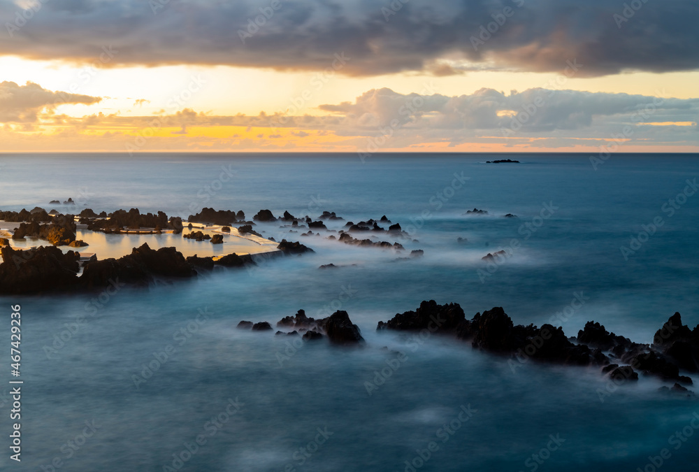 Porto Moniz on the north coast of Madeira island Portugal with a popular natural complex of lava pools perfect for bathing. Dusk sunset seascape panorama with black volcanic rocks, longtime exposure.