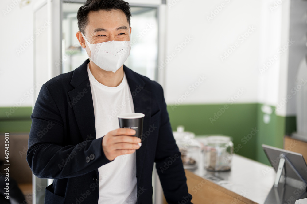 Asian businessman in medical with coffee going in store. Concept of health protection during Coronavirus pandemic. Modern adult successful male person wearing suit Asian businessman in medical with coffee going in store. Concept of health protection during Coronavirus pandemic. Modern adult successful male person wearing suit