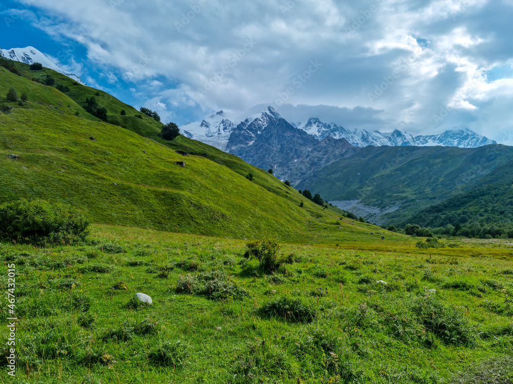 A panoramic view on the snow-capped peaks of Tetnuldi, Gistola and Lakutsia in the Greater Caucasus Mountain Range in Georgia, Svaneti Region. Hills with lush pastures, sharp peaks, wanderlust.
