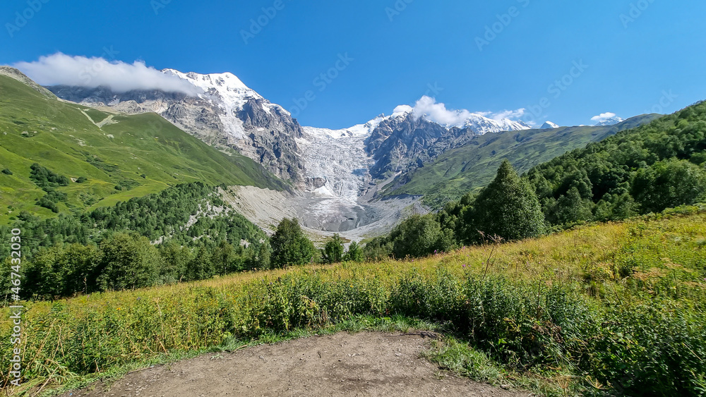 Obraz premium A panoramic view on the snow-capped peaks of Tetnuldi, Gistola, Lakutsia and the Adishi Glacier in the Greater Caucasus Mountain Range in Georgia, Svaneti Region. Sharp peaks, wanderlust, solitude.
