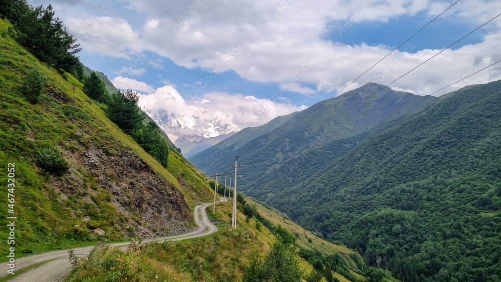 A mountain road in the Greater Caucasus Mountain Range in Georgia, Svaneti Region. Electricity lines are built up along the valley. In the background are sharp snow-capped mountains. Adventure,Freedom