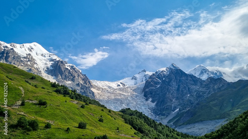 A panoramic view on the snow-capped peaks of Tetnuldi, Gistola and Lakutsia in the Greater Caucasus Mountain Range in Georgia, Svaneti Region. Hills with lush pastures, sharp peaks, wanderlust.