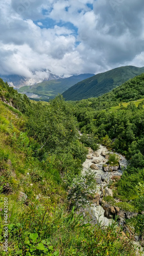 A panoramic view on the cloud covered peaks of Tetnuldi, Gistola and Lakutsia in the Greater Caucasus Mountain Range in Georgia, Svaneti Region. River Adishischala flowing down the valley.