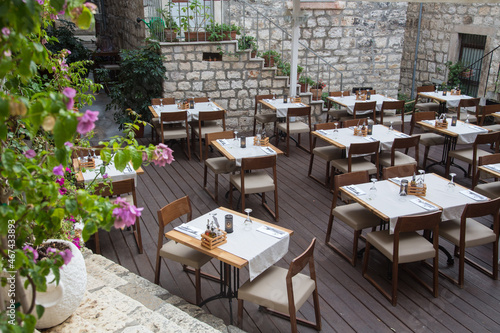 Fototapeta Naklejka Na Ścianę i Meble -  Inviting tables of an outdoor terrace restaurant decorated with fabric table cloths and napkins waiting for guests or tourists within medieval walls in Croatia