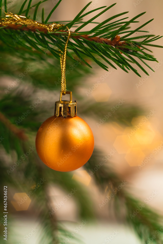 A beautiful golden ball hangs on a Christmas tree on a blurred shiny background. Christmas decor. A beautiful golden ball hangs on a Christmas tree on a blurred shiny background. Christmas decor.