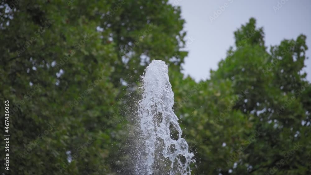 Close up of stream of fountain water splashes against blurred green background. Slow motion. 