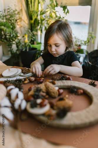 A little girl makes a wreath from natural materials. Autumn needlework with handmade children