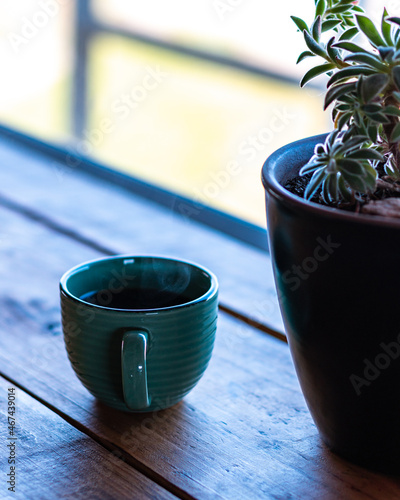 Vertical view of a steaming cup of coffee on a wooden table and a succulent plant on the right.