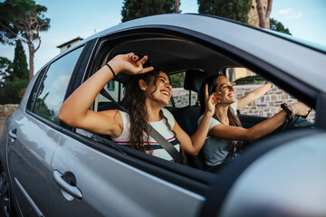 Two young women sing a song on the radio and dance in the car on a day trip in the summer - Best friends having fun together driving around the countryside - Smiling millennial in a relaxing moment