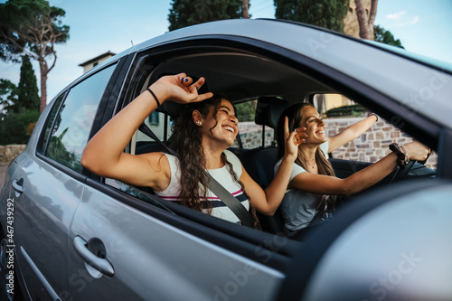 Two young women sing a song on the radio and dance in the car on a day trip in the summer - Best friends having fun together driving around the countryside - Smiling millennial in a relaxing moment photo